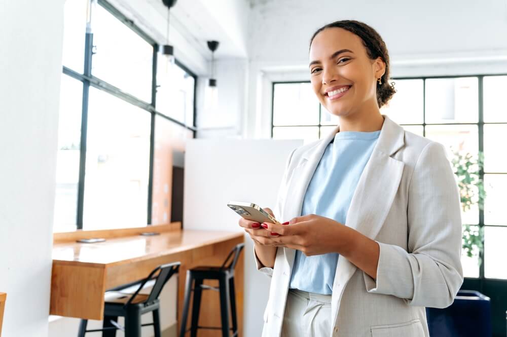 shutterstock_2237878213 (1) Woman smiling while holding a mobile phone